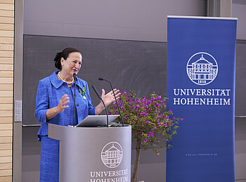 Eine Frau steht in einem Auditorium an einem Pult und hält eine Rede.