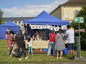 Vor einem Partyzelt stehen Menschen und freuen sich auf asiatisches Essen, das dort verkauft wird.