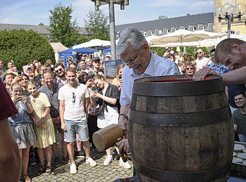 Ein Mann beim Fassanstich wird von vielen Menschen beobachtet und fotografiert.